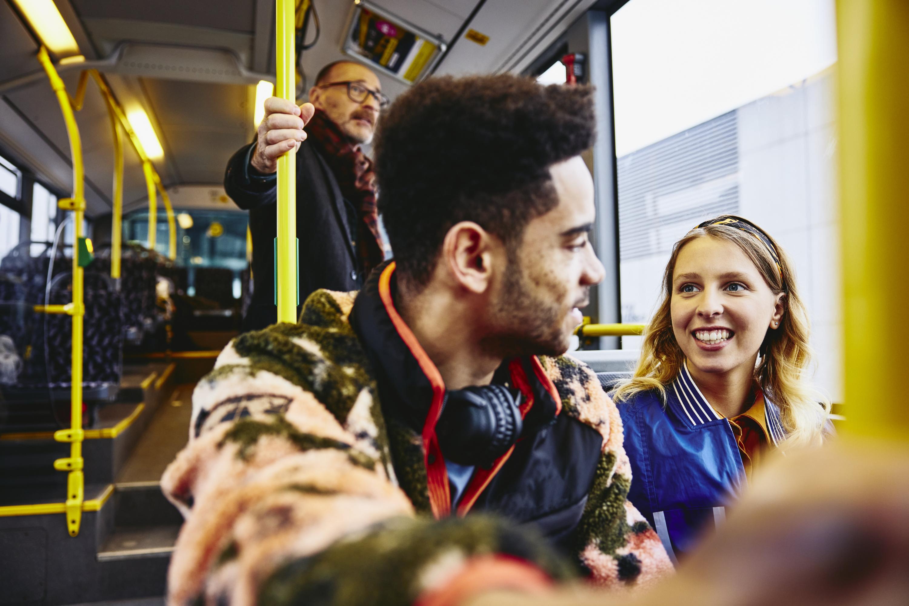 Woman and boy having a conversation, smiling, sitting in a bus. Other people in the background.