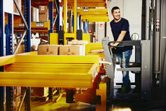 Smiling male standing on a forklift.