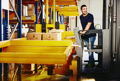 Smiling male standing on a forklift.