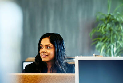 Kvinne ved pulten sin, bak datamaskinen