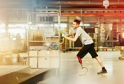male pushing a trolley with packages through a warehouse.
